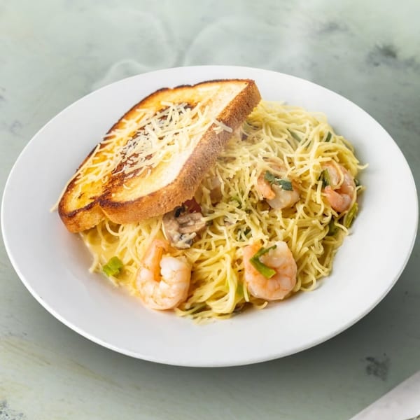 Shrimp scampi with angel hair pasta, mushrooms, green onions, and a slice of cheesy garlic bread.