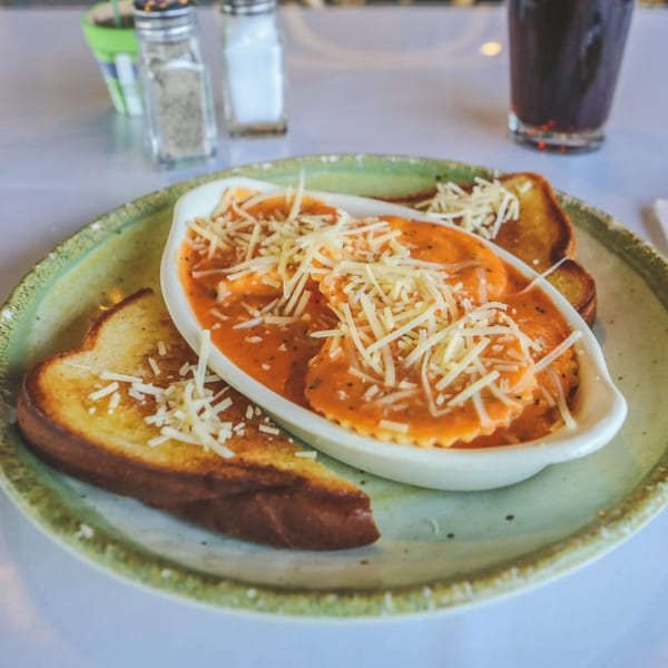 Ravioli in tomato sauce topped with shredded cheese, served with toasted bread on a green plate.