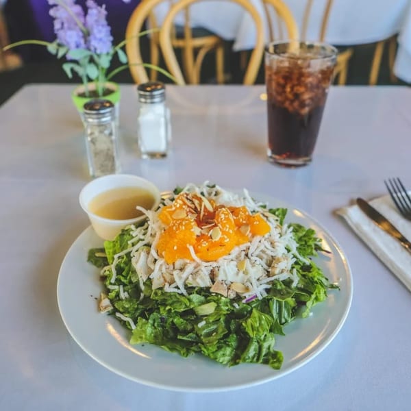 A Greenhouse Cafe salad with lettuce, chicken, mandarin oranges, almonds, and dressing on a white table.
